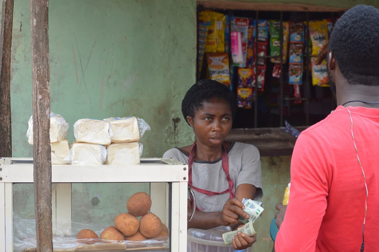 A shopkeeper hands change to a customer across the counter of a small provision store.
