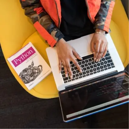 Hands typing on a laptop balanced on a yellow chair.